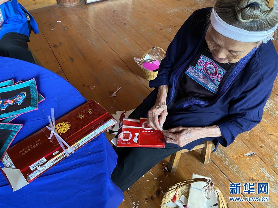侗繡技藝傳承人、今年94歲的覃奶時清在裁剪侗繡圖案。