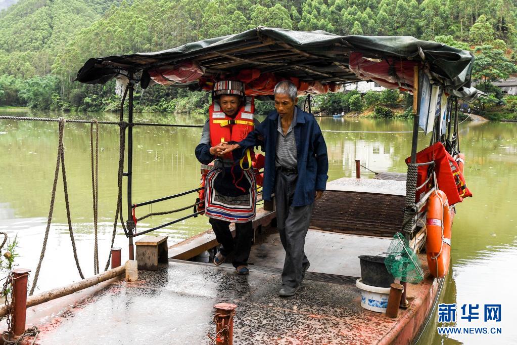 趙仕斌（左）攙扶腿腳不便的村民下船。